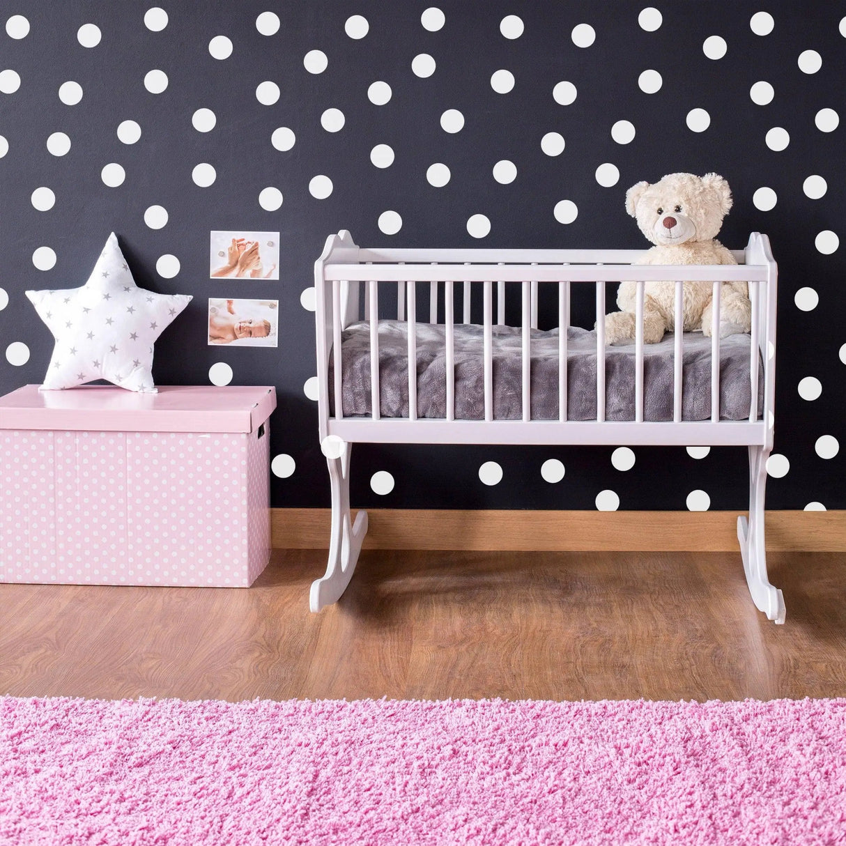Cozy nursery with white round dot stickers on black wall, a crib, pink rug, and a teddy bear for a creative touch.