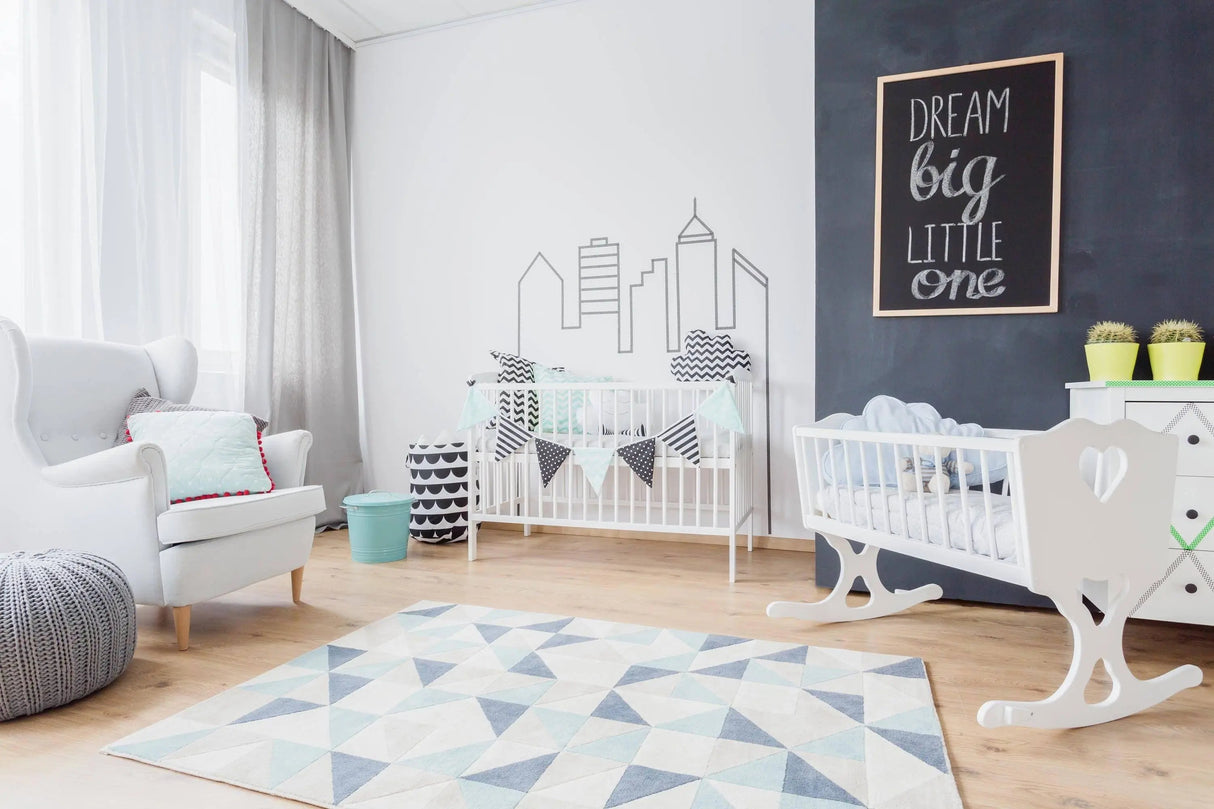 Stylish nursery with white cribs, modern decor, and a motivational wall art saying 'Dream Big Little One'.