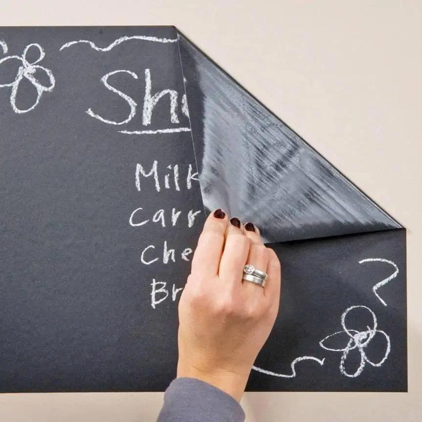 Person peeling back a chalkboard wall decal with a shopping list written on it, showcasing its creative versatility.