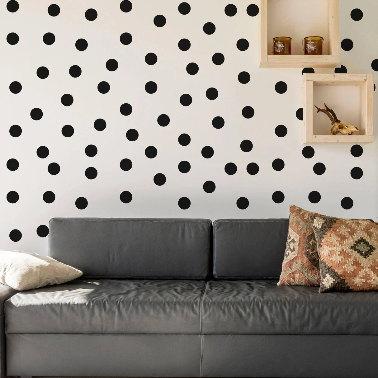 Small black circle wall stickers decor on a white wall above a stylish gray couch with decorative pillows.