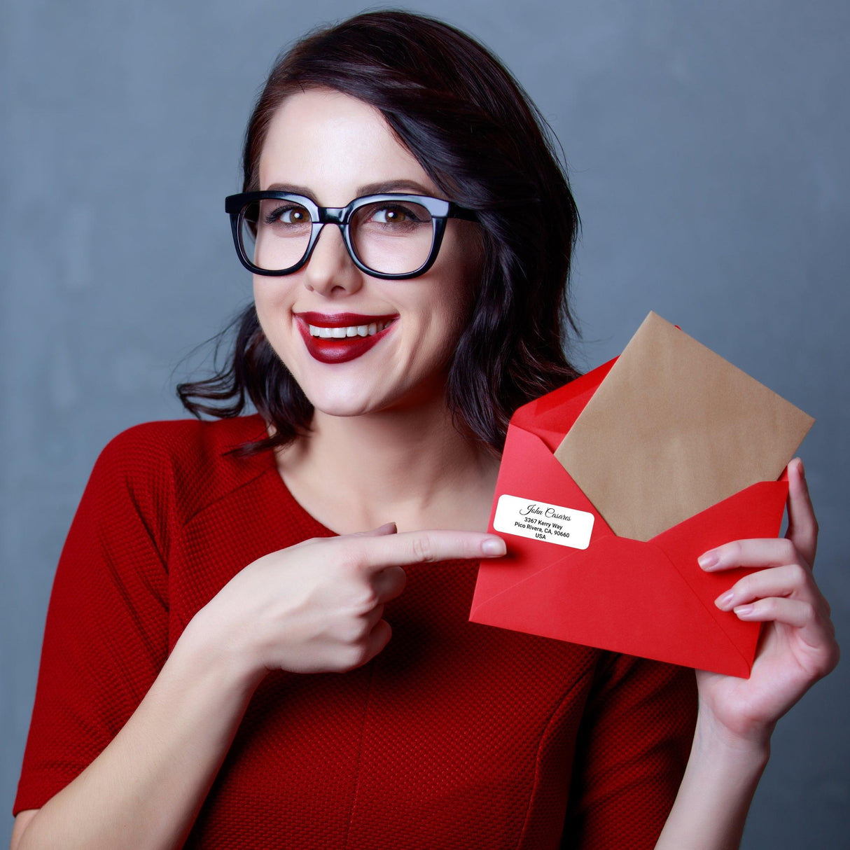 Woman in red shirt pointing at a custom clear mailing label on a red envelope.