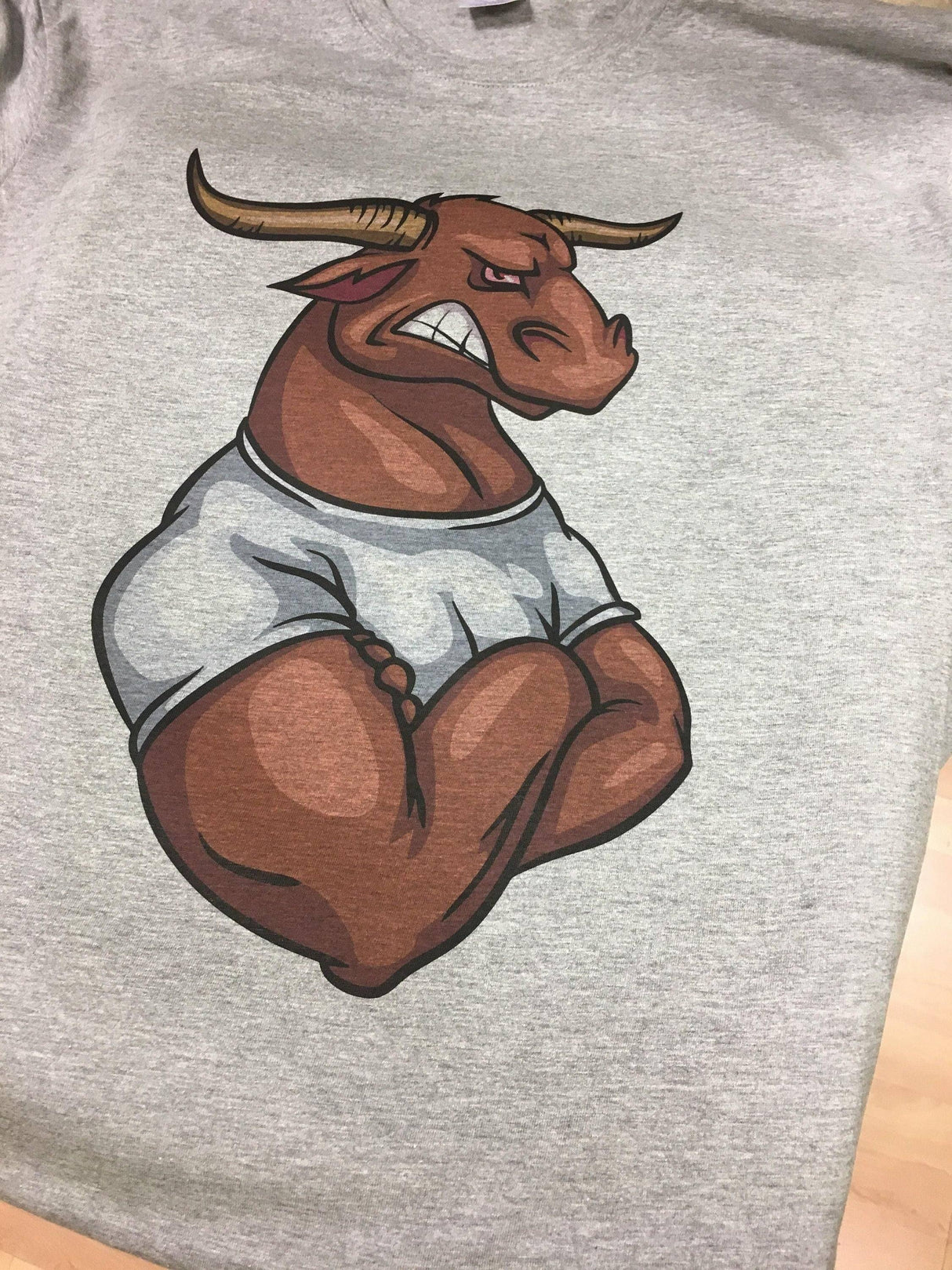 Graphic design of an angry bull in a white t-shirt on a gray background, showcasing a unique t-shirt artwork.