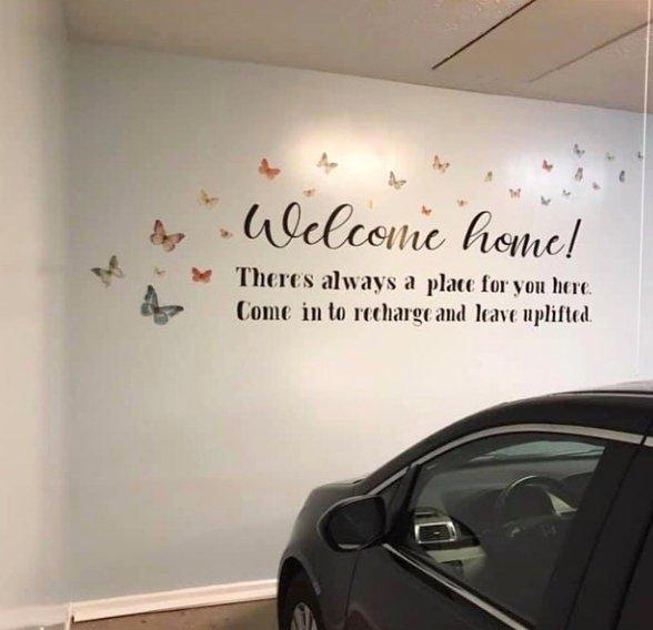 Wall mural with the text 'Welcome home! There's always a place for you here. Come in to recharge and leave uplifted' decorated with butterflies.