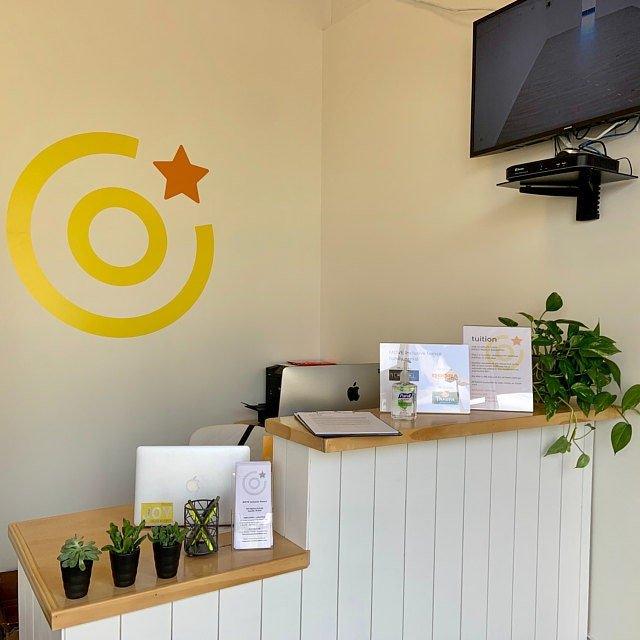 Bright reception area with yellow wall art, desk, plants, and informational signage.