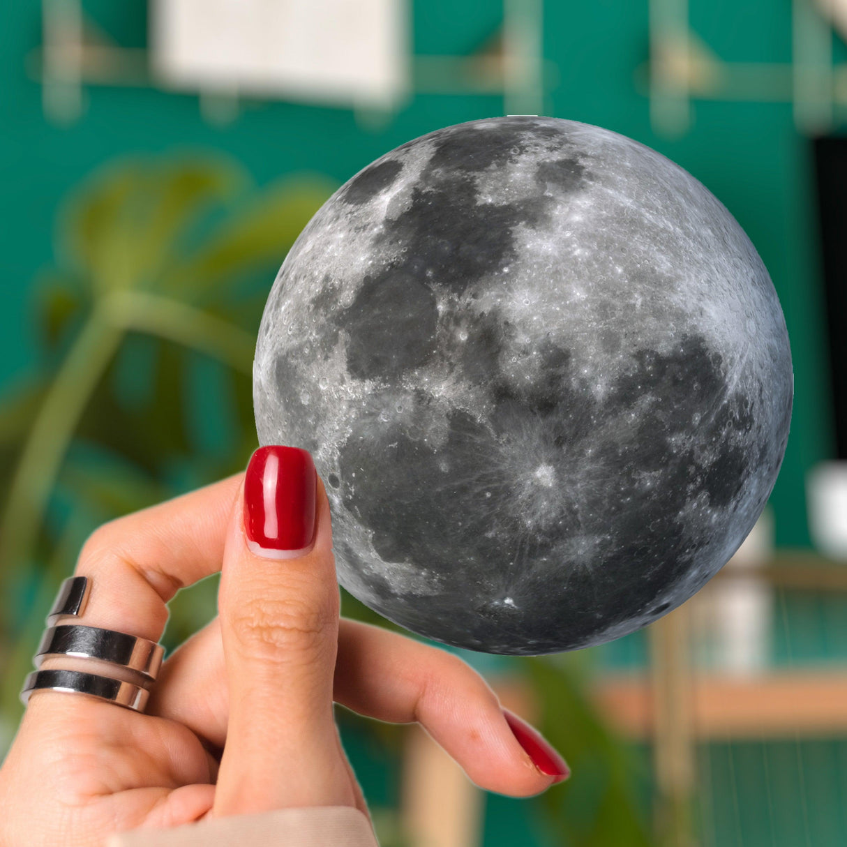 Hand holding a realistic moon-shaped decal against a green background, perfect for glowing laptop accents.
