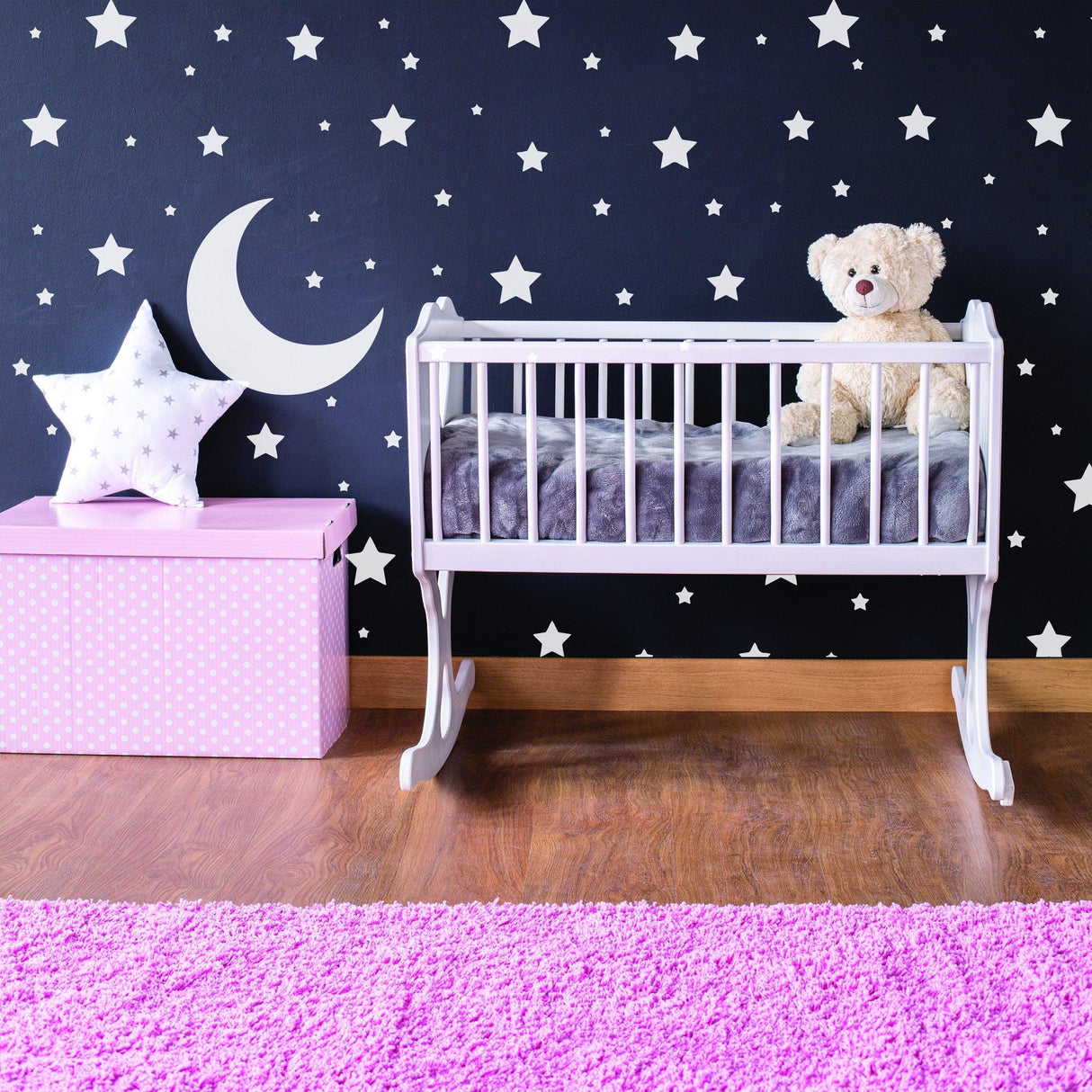 Cozy nursery with white stars and moon wall stickers, a crib, teddy bear, and pink decor.