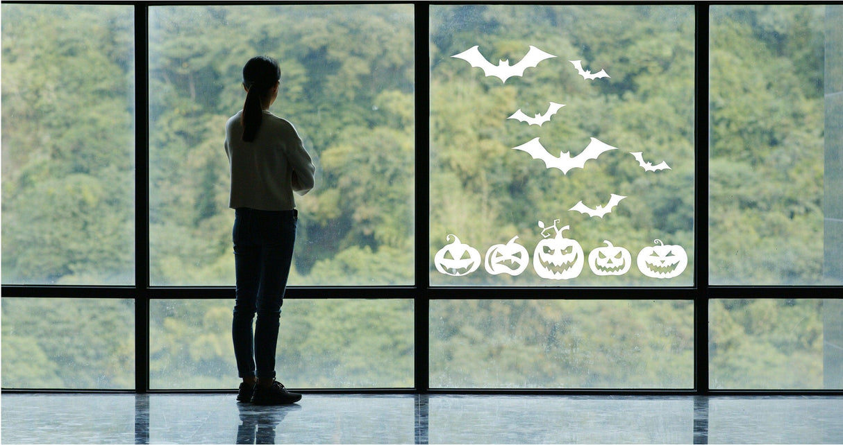 Person admiring Halloween window decals with pumpkins and bats on a large glass window.
