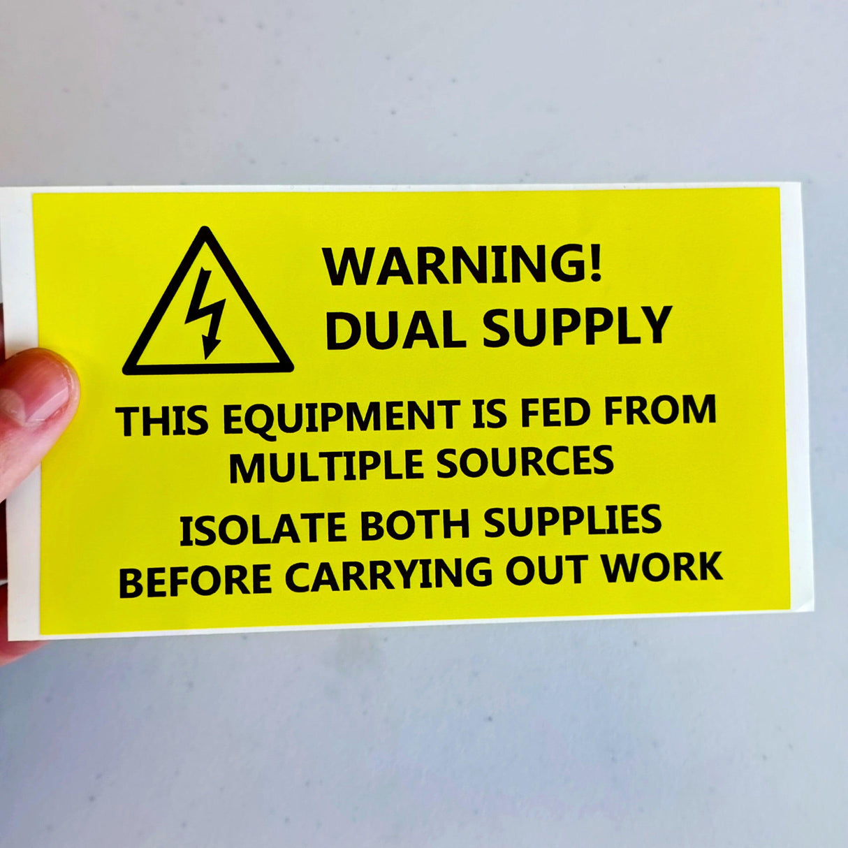 Bright yellow Dual Supply Warning Label sticker displaying safety precautions for electricians.