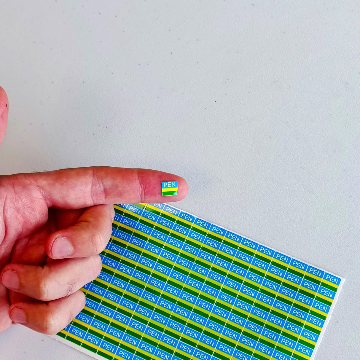 Hand holding a small PEN marking sticker on a background of multiple PEN electrical component labels.