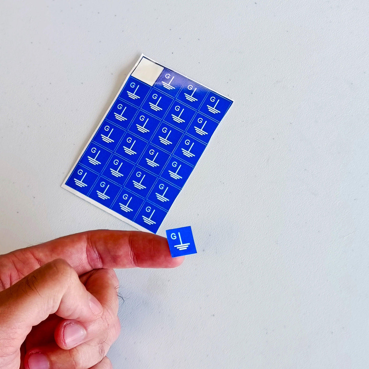 Blue grounding symbol stickers held between fingers, showing square 'G' labels for electrical safety.