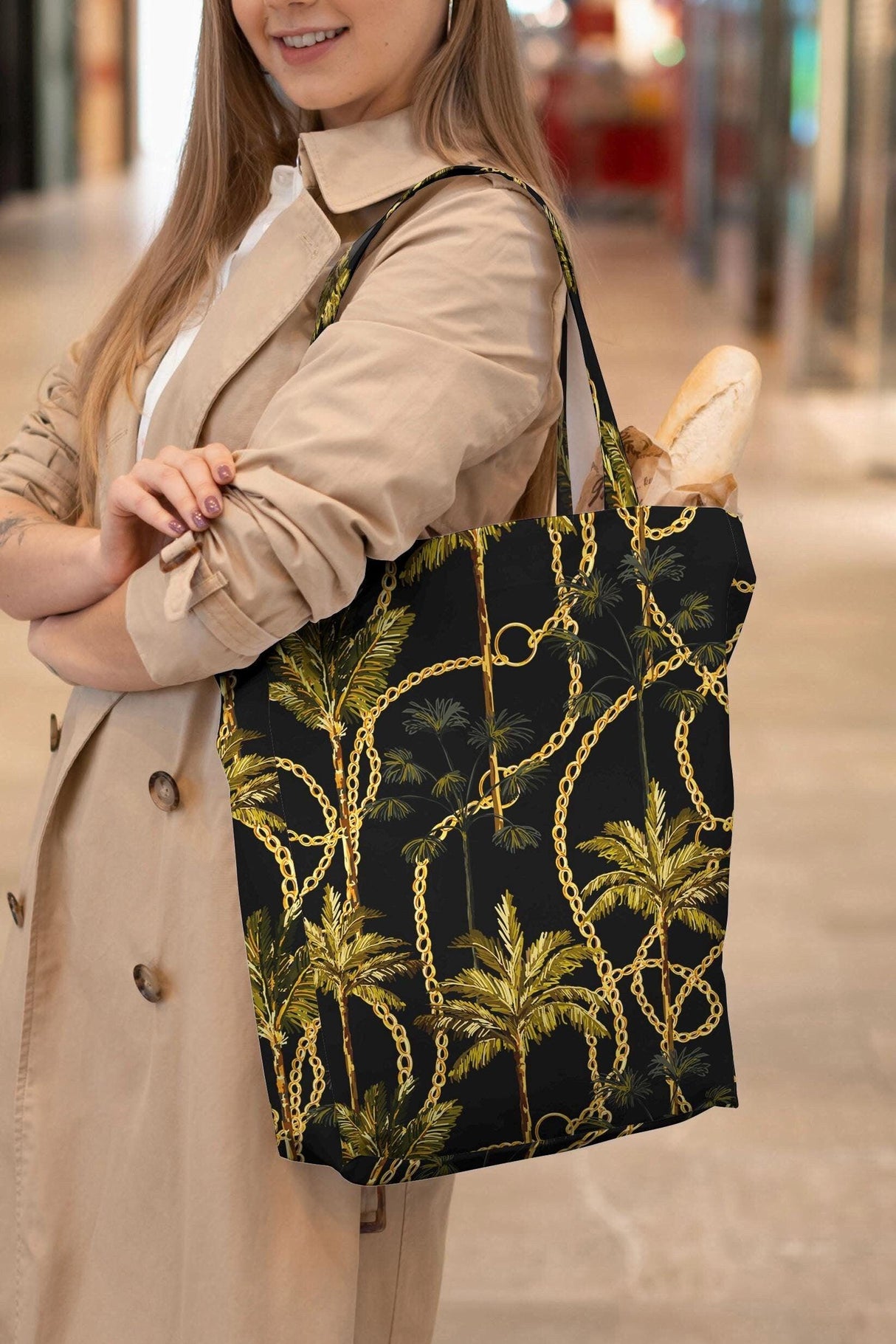 Woman in a beige trench coat carrying a stylish black shopper bag with a gold chains and palm trees design.