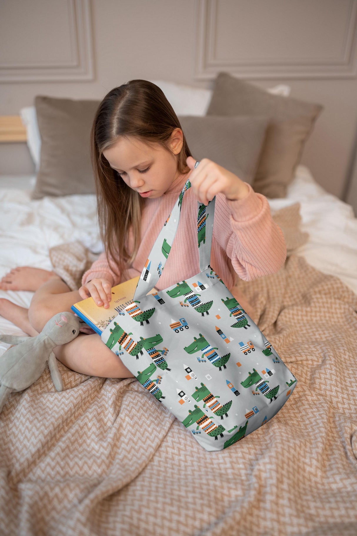 Girl using a grey dinosaur and cars tote bag while reading, showing eco-friendly design and playful style.