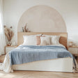 Minimalist boho bedroom with beige semi-circle wall decal and wooden bed frame, featuring soft bedding and elegant decor.