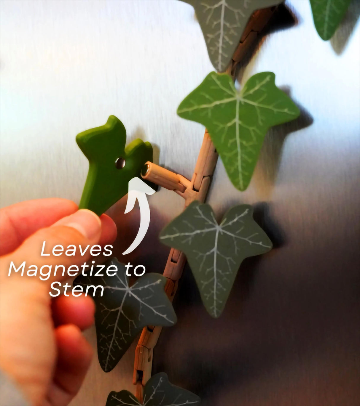 Hand attaching a green leaf magnet to the articulated stem of an English Ivy fridge magnet decor.