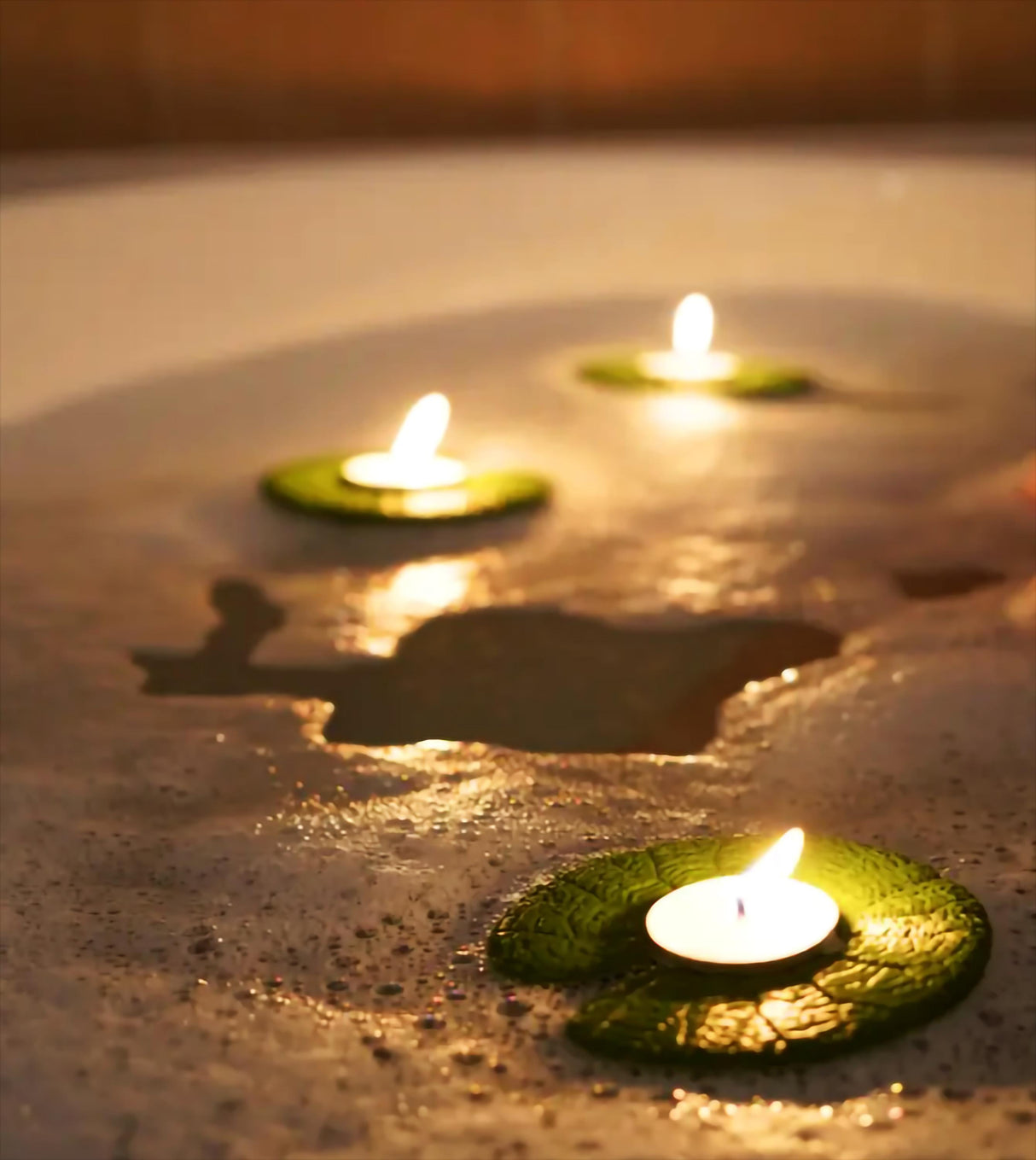 Floating lily pad candle holders glowing in a relaxing bath setting, enhancing spa ambiance.