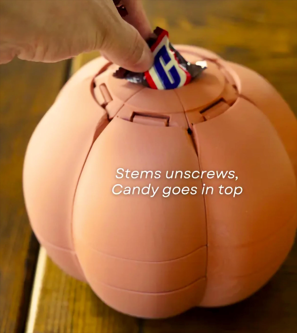 Hand placing candy into the top of a Smack O'Lantern Halloween candy bowl, showcasing its unique design.
