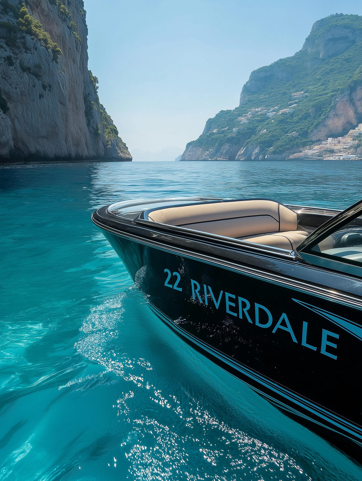 Custom boat with personalized decal '22 RIVERDALE' cruising in clear blue water near rocky cliffs.