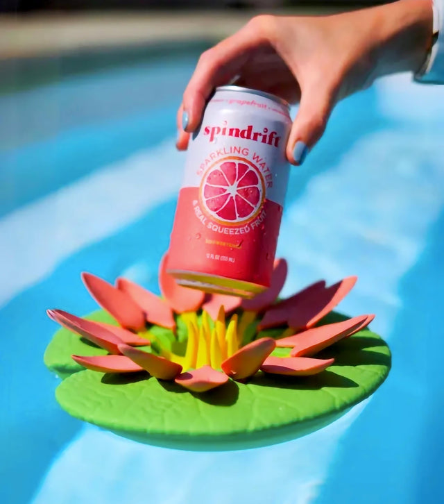 Hand holding a can of sparkling water on a floating lily pad drink holder in a pool.