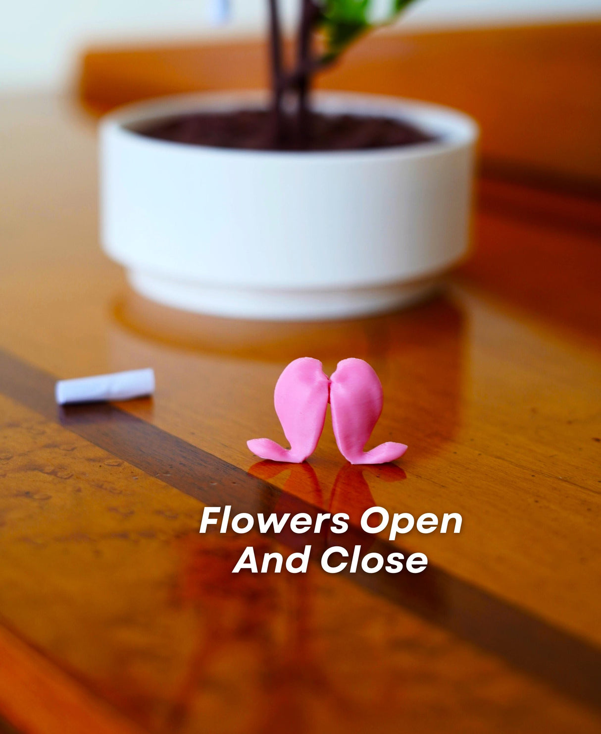 Close-up of pink 3D flowers resembling blooming hearts, next to a love note, on a wooden table.