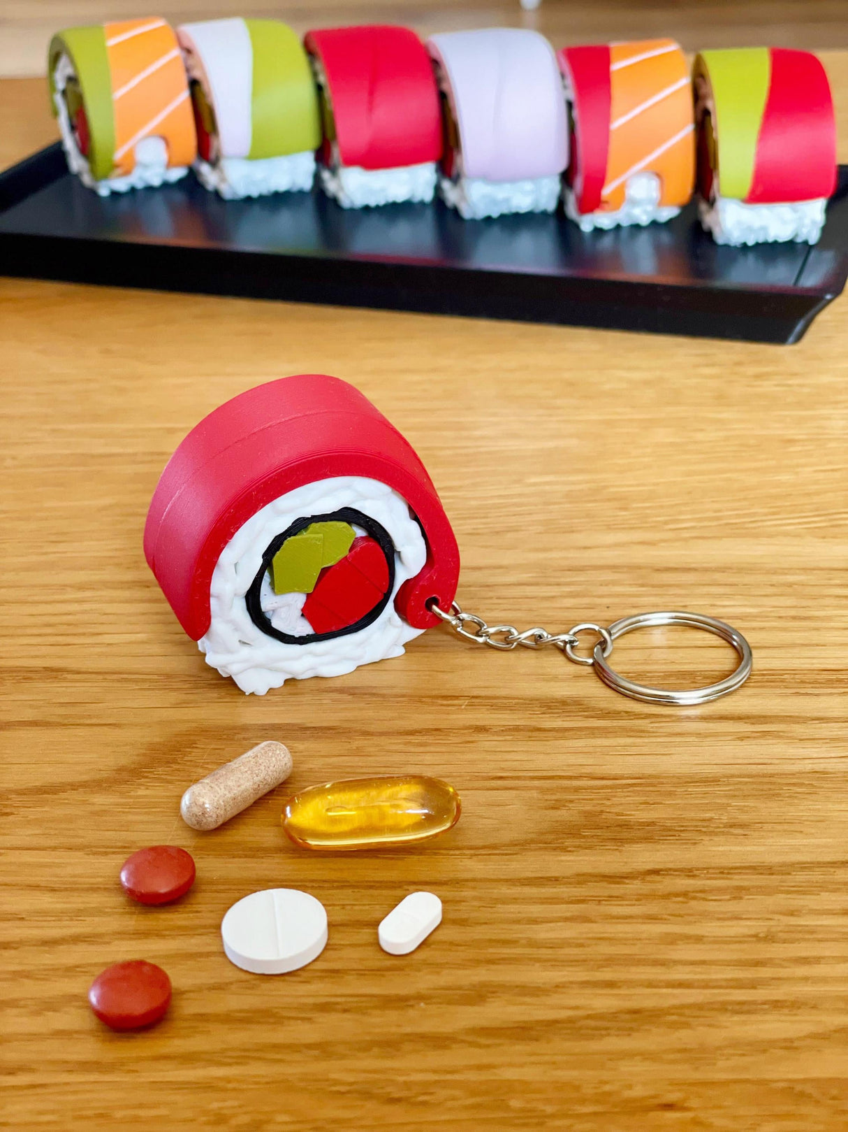 Sushi pill organizer keychain with weekly supplement containers on a wooden table, colorful sushi design.