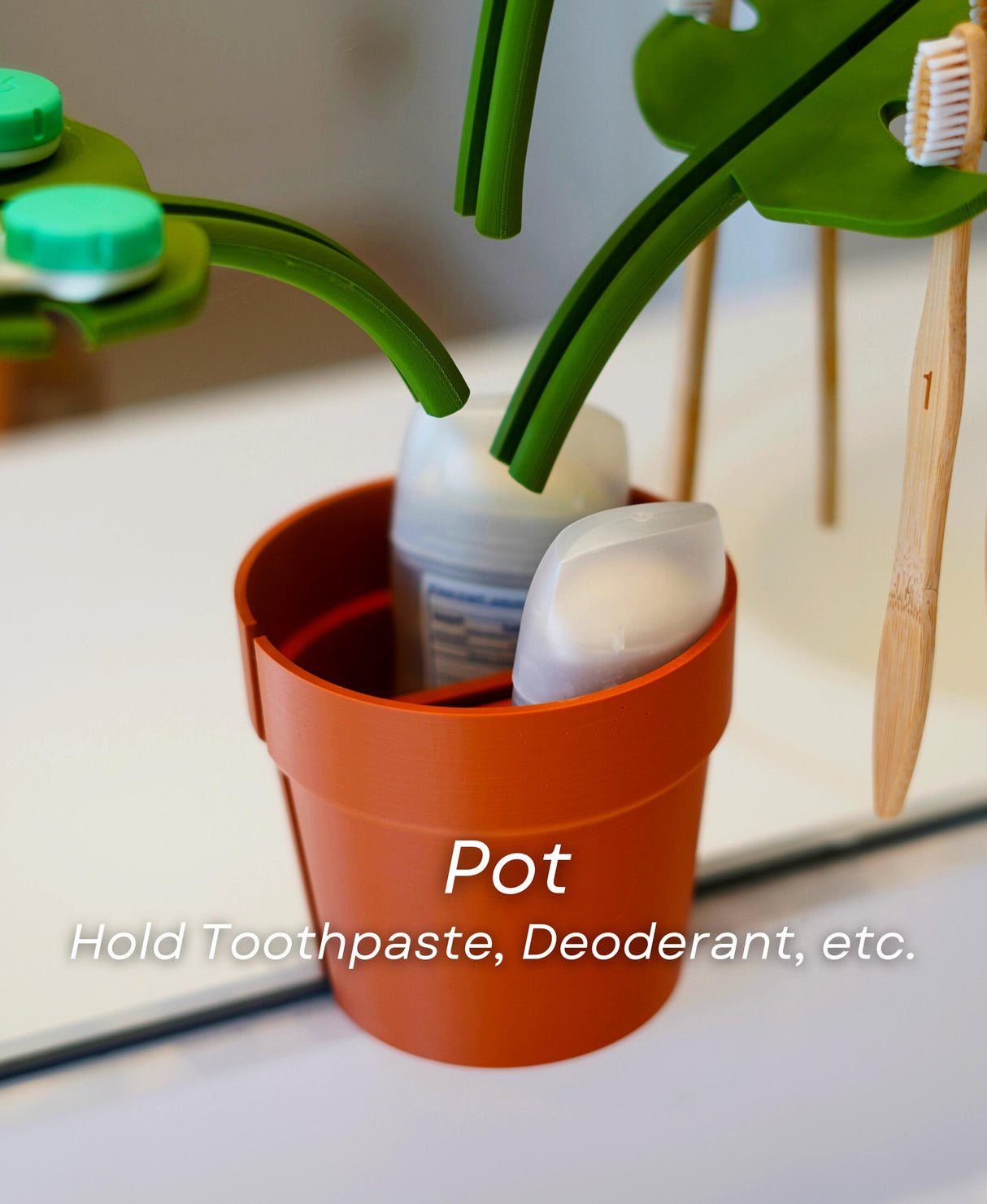 Mirror Monstera organizer pot holding toothpaste and deodorant, functional bathroom storage solution.