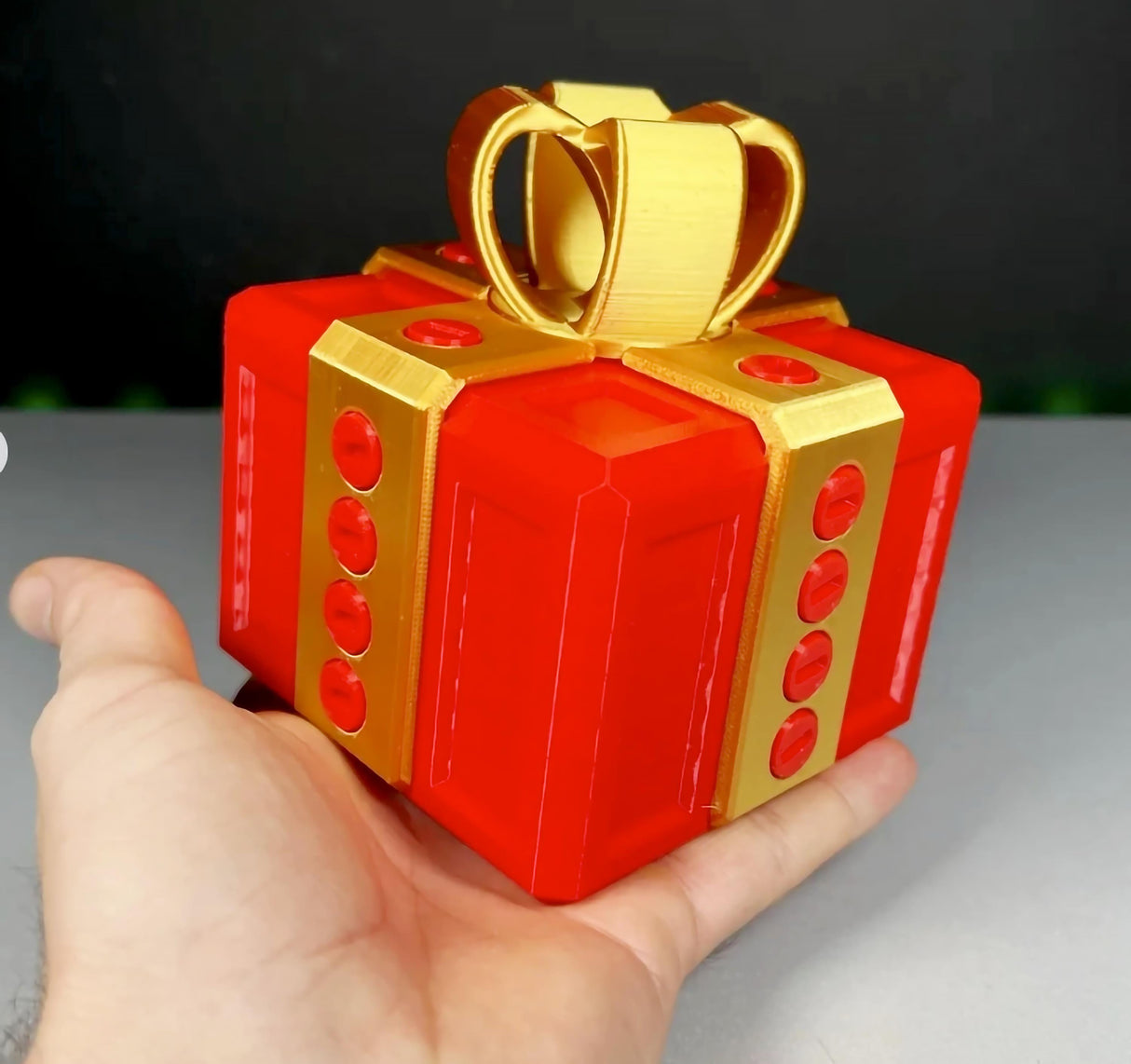 Mini Annoying Gift Box in hand, 3D printed puzzle with a vibrant red design and golden bow, perfect for funny gag gifts.