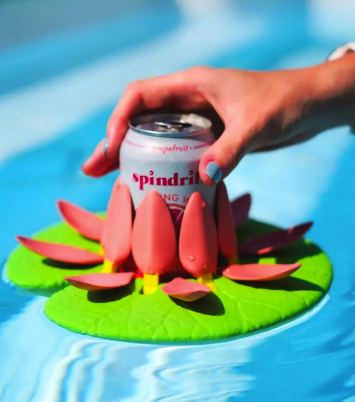 Hand holding a can in a colorful lily pad cupholder floating in a pool, featuring 3D-printed petals.