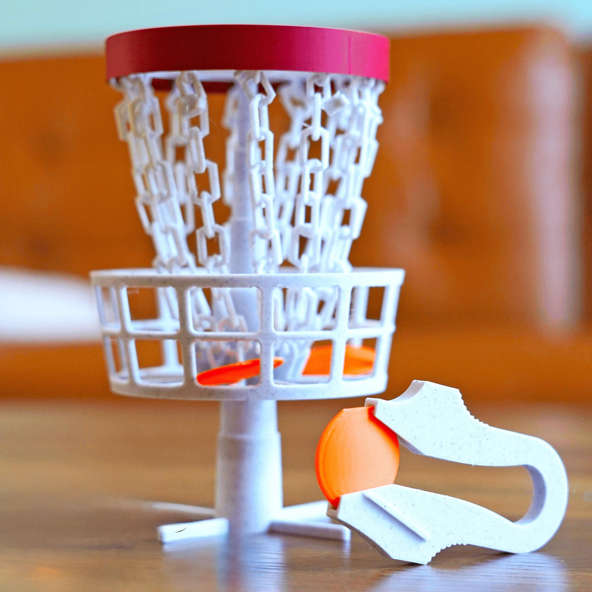 Mini disc golf basket with chains and an orange disc, perfect for trick shots and desktop fun.