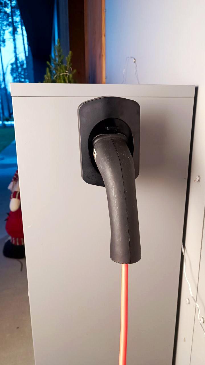 Electric car charger connector holder mounted on a wall with charging cable attached.