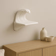 3D printed wave-shaped floating shelf in matte white, featured on a wooden surface, enhancing minimalist decor.