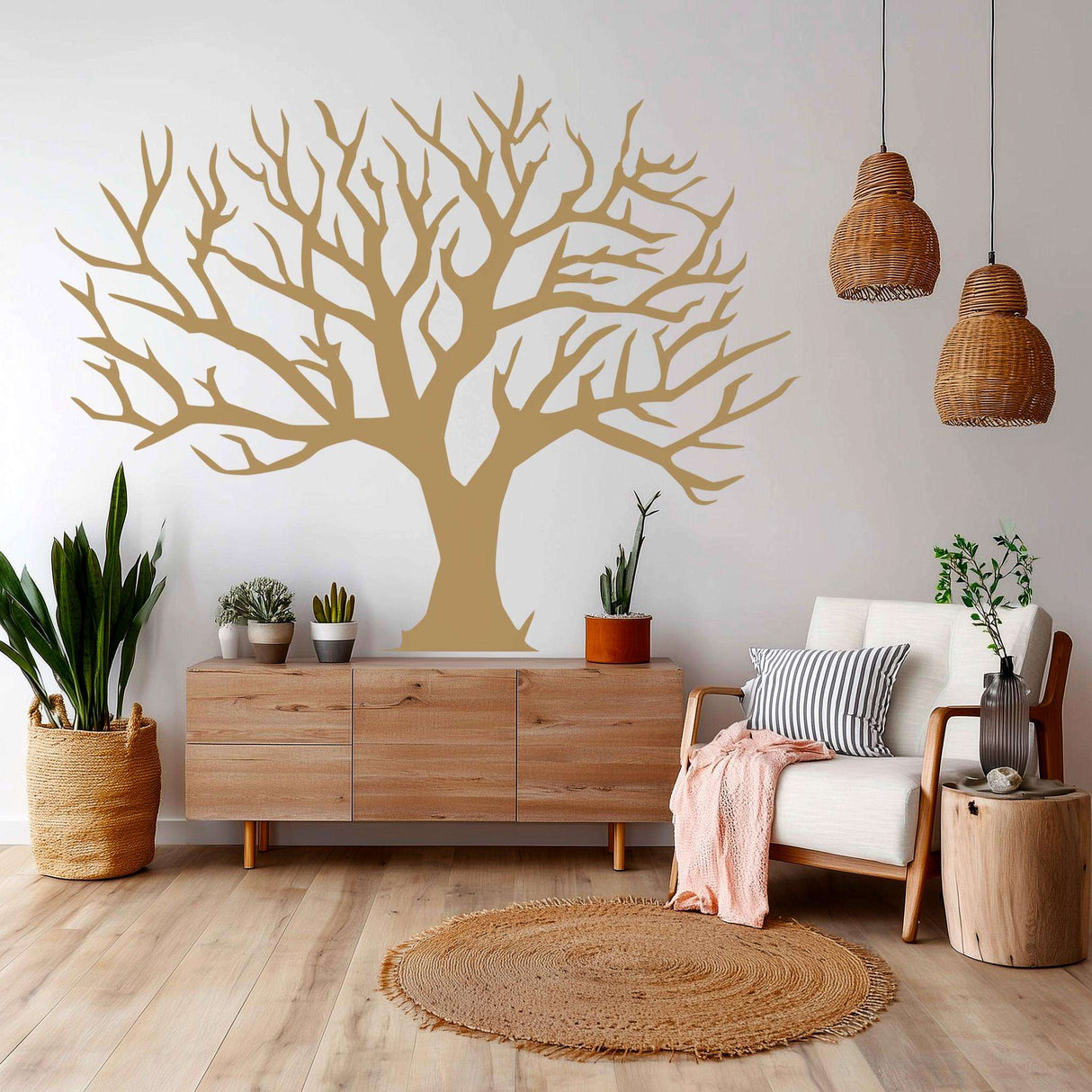 A large, leafless tree wall decal in a soft neutral tone, applied in a cozy, boho-style living room with wood and rattan accents, light flooring, and natural indoor plants. The decal gives the appearance of a painted mural.