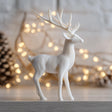 3D printed minimalist reindeer figurine made of matte PLA plastic, placed on wooden surface with soft festive lighting in background