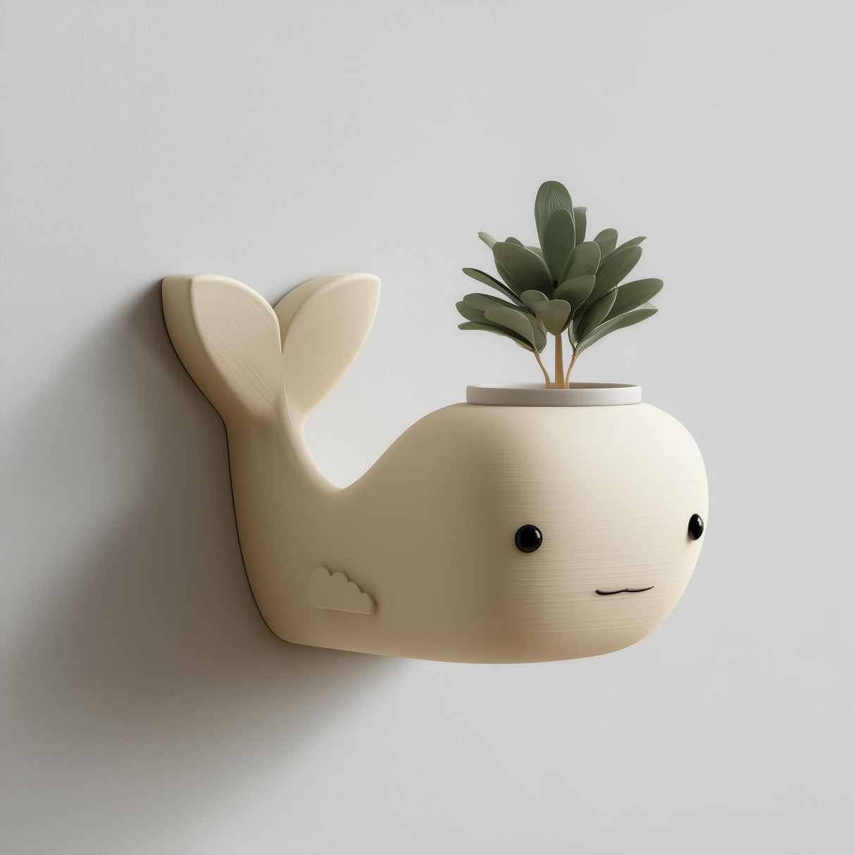 3D printed matte PLA wall-mounted whale-shaped planter with a small plant growing from an opening in the top, hanging on a light-colored wall.