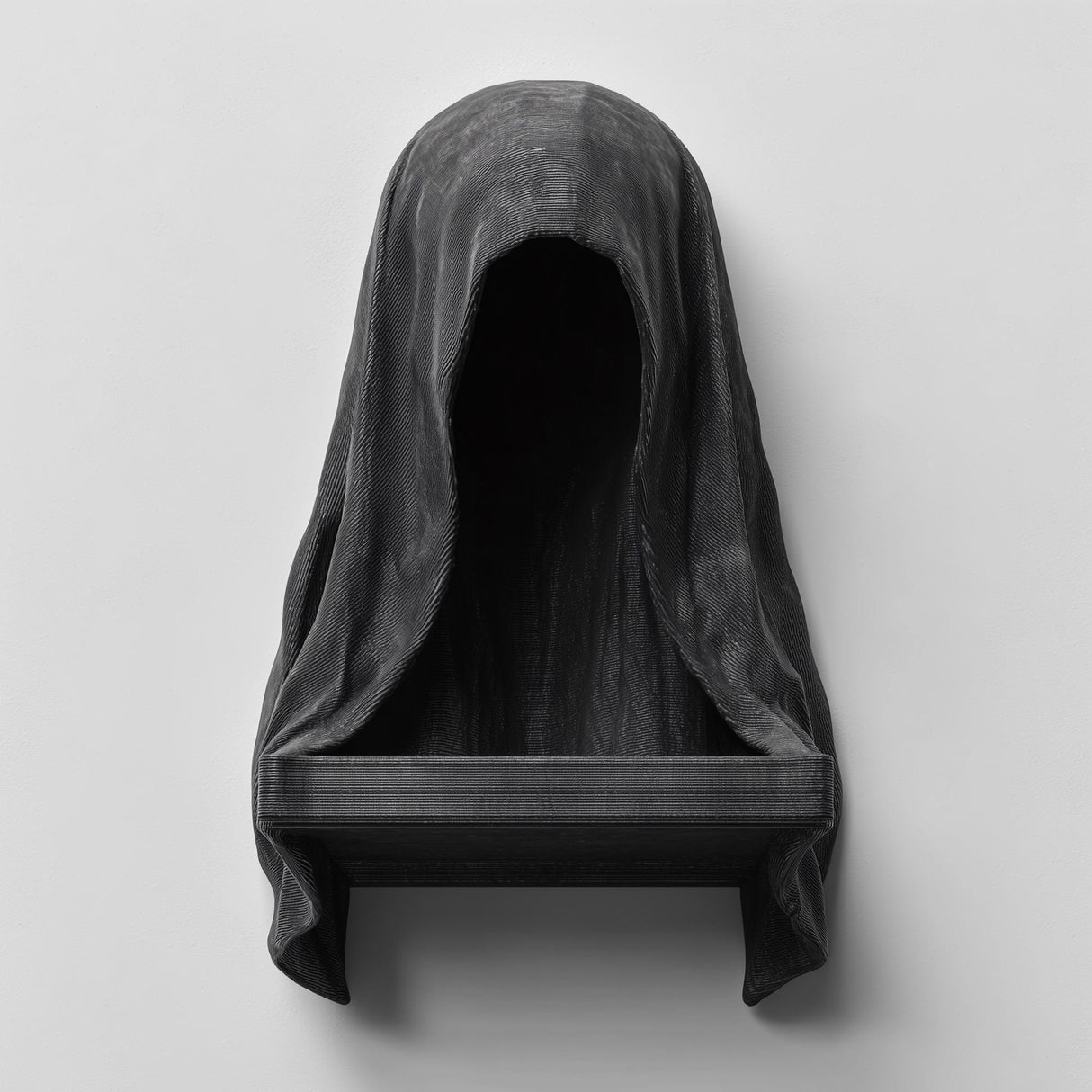 3D printed matte black wall shelf shaped like a hooded cloaked figure with a dark empty face and a small ledge at the bottom, mounted on a light wall.
