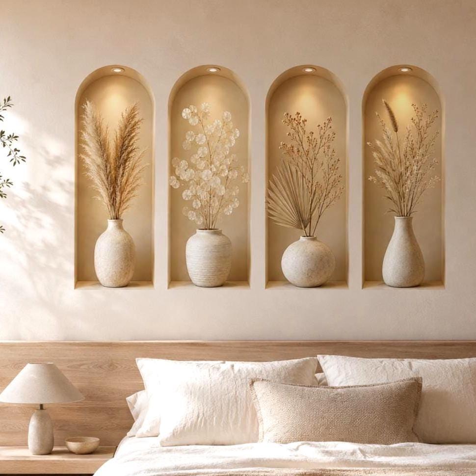 Four tall arched beige wall niches with warm overhead spotlights, each displaying a cream ceramic vase filled with a different dried botanical arrangement in soft neutral tones.