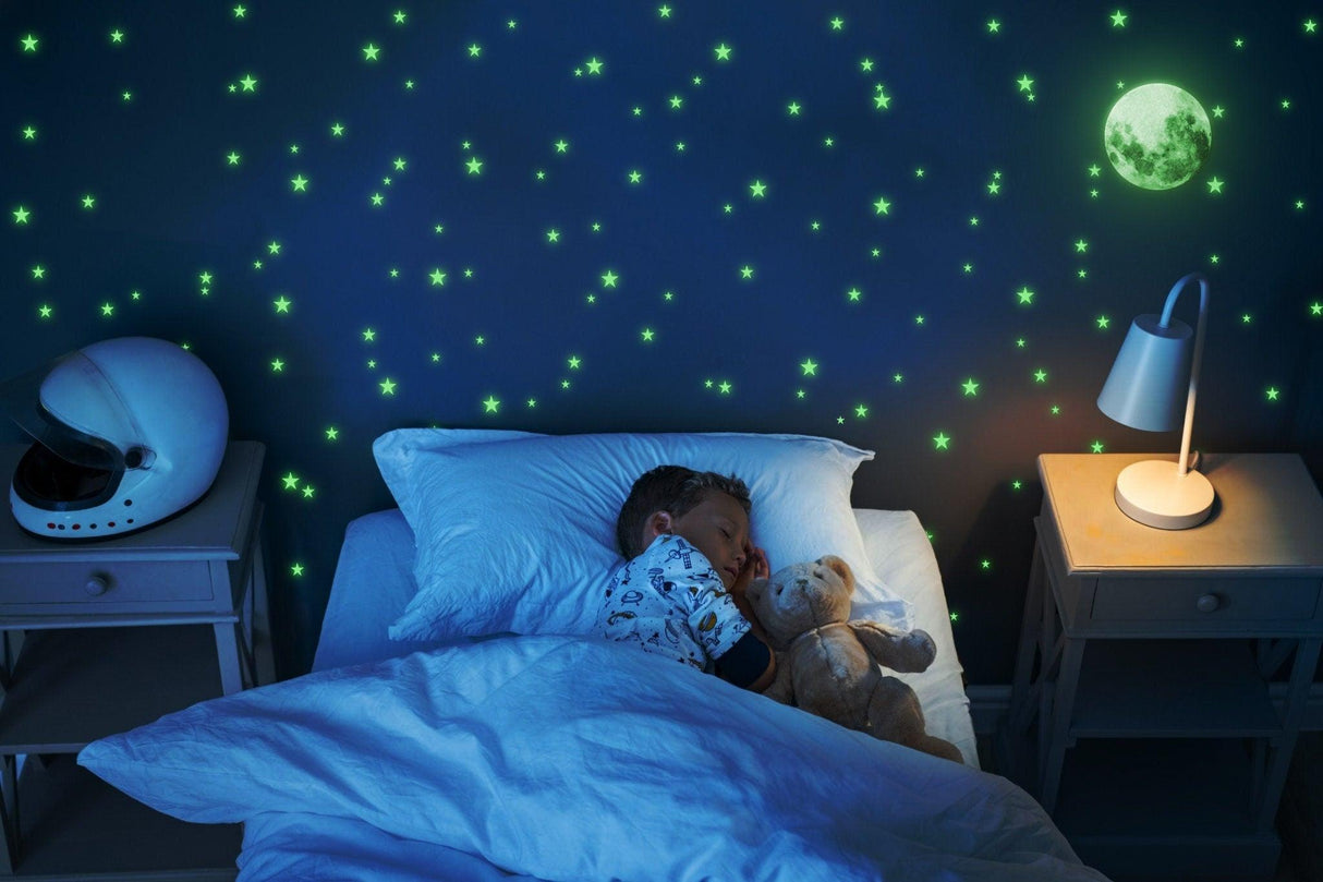 Child sleeping peacefully under glowing star decals and moon on the wall, creating a magical night sky ambiance.