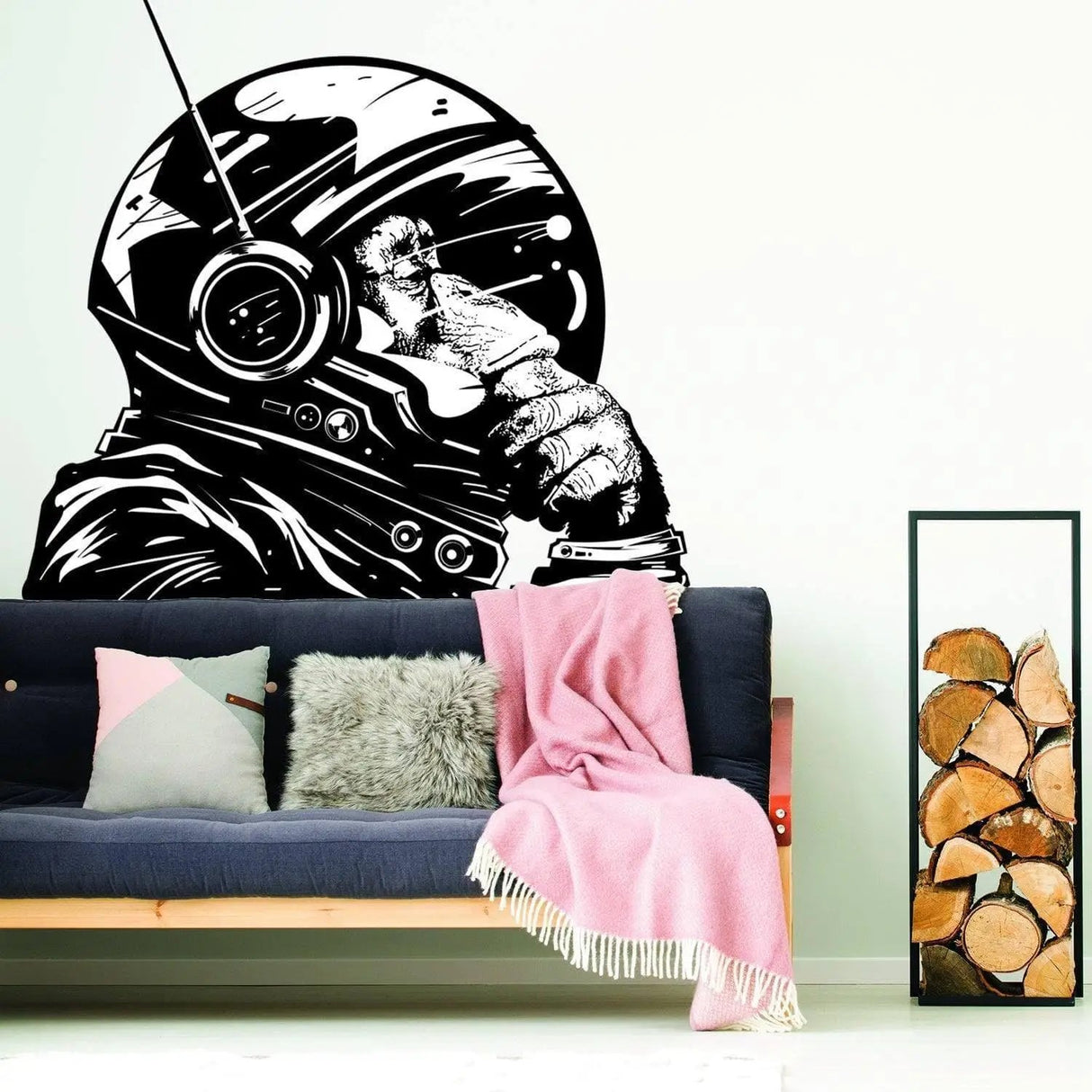 Monkey astronaut wall decal on white wall above a couch with pink blanket and decorative logs.