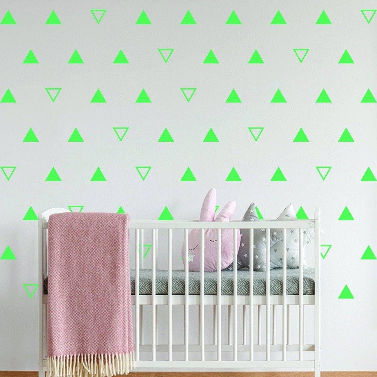Bright green triangle wall decals in a child's nursery with a crib, pink blanket, and decorative pillows.