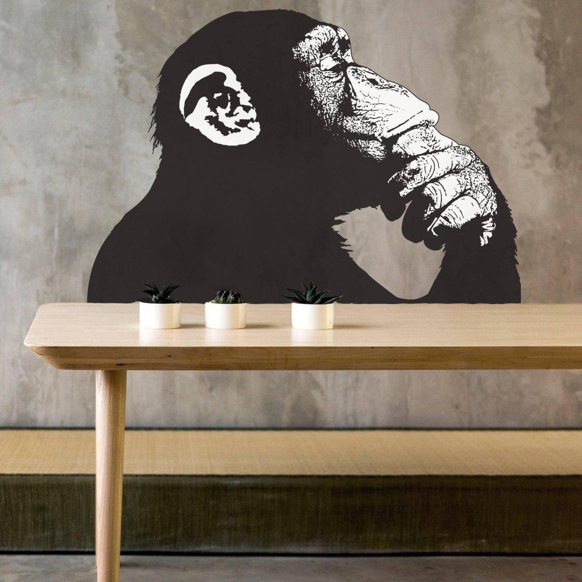 Contemporary street art primate decal of a thinking monkey on a wall above a wooden table with plants.