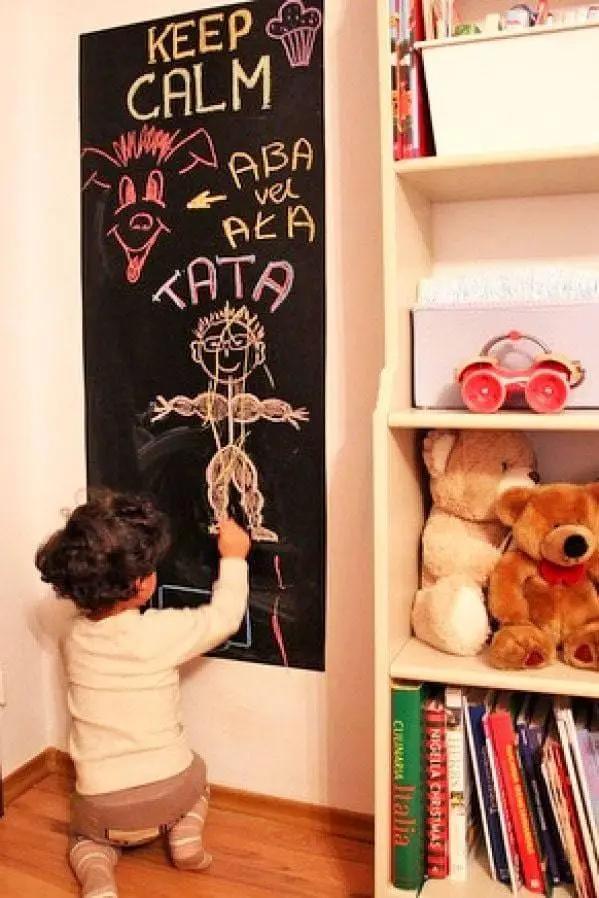 Child drawing on a blackboard wall sticker, showcasing creativity and fun in a cozy home environment.
