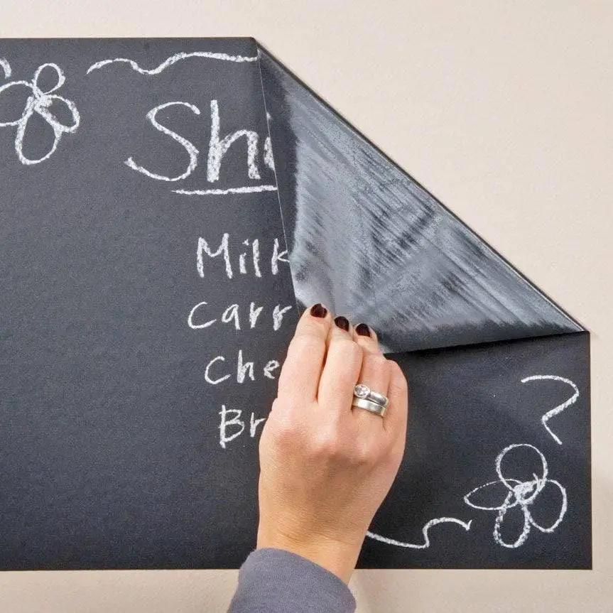 Person applying a chalkboard wall sticker with chalk-written grocery list in a kitchen setting.