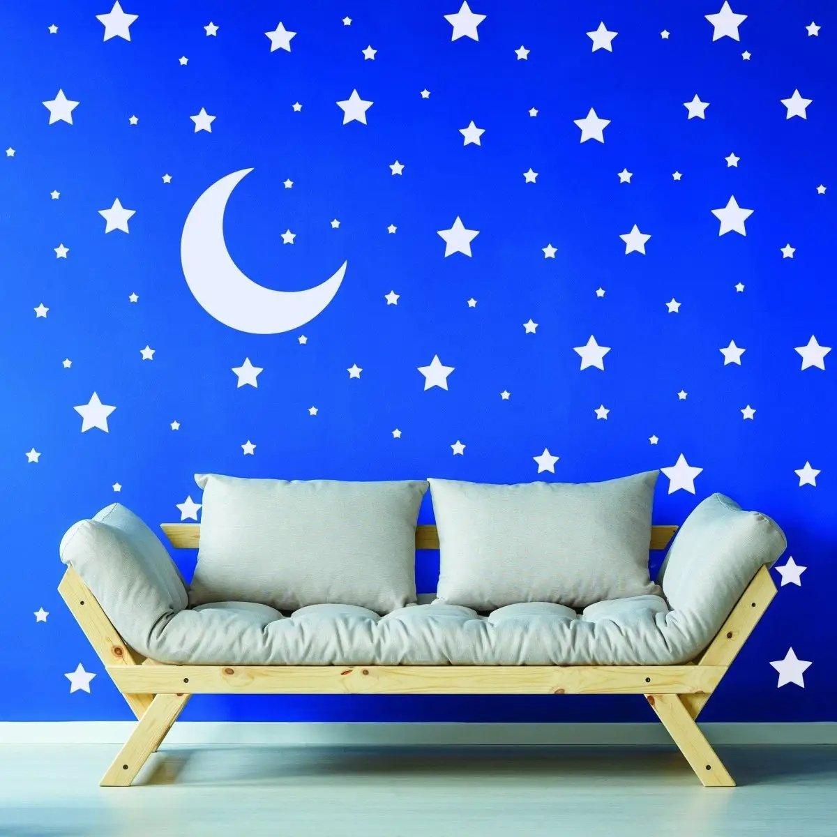 Celestial Dreams wall sticker collection featuring white stars and moon on blue wall above a cozy wooden sofa.