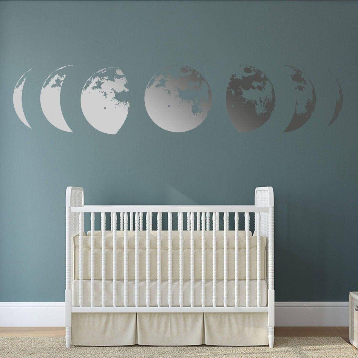 Moon phase wall sticker decor above a white crib in a nursery with a calming dark blue wall.