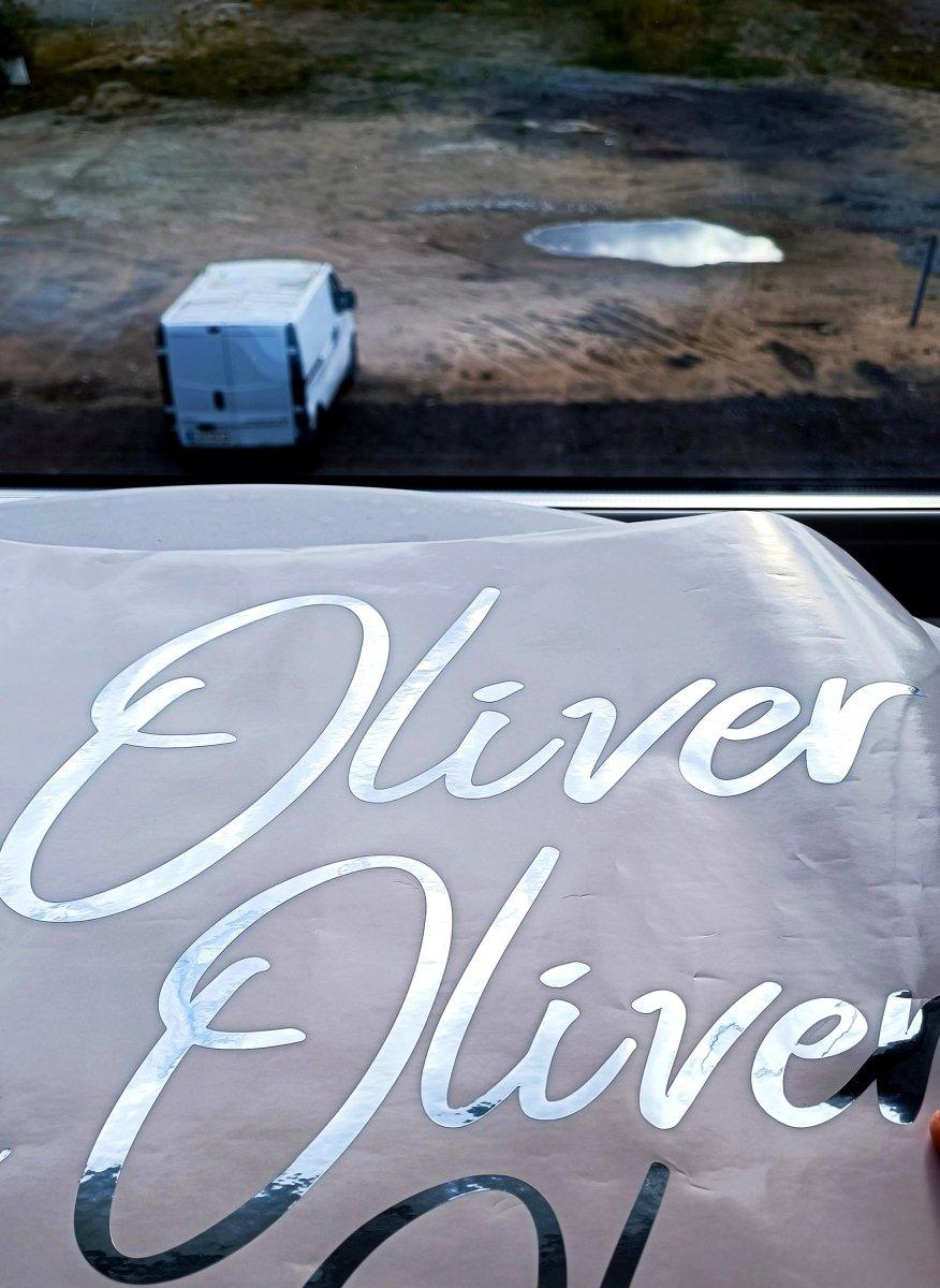 Personalized silver chrome vinyl name decal reading 'Oliver' against an outdoor backdrop.