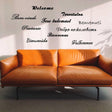Wall decal with 'Welcome' in multiple languages above a modern brown couch.
