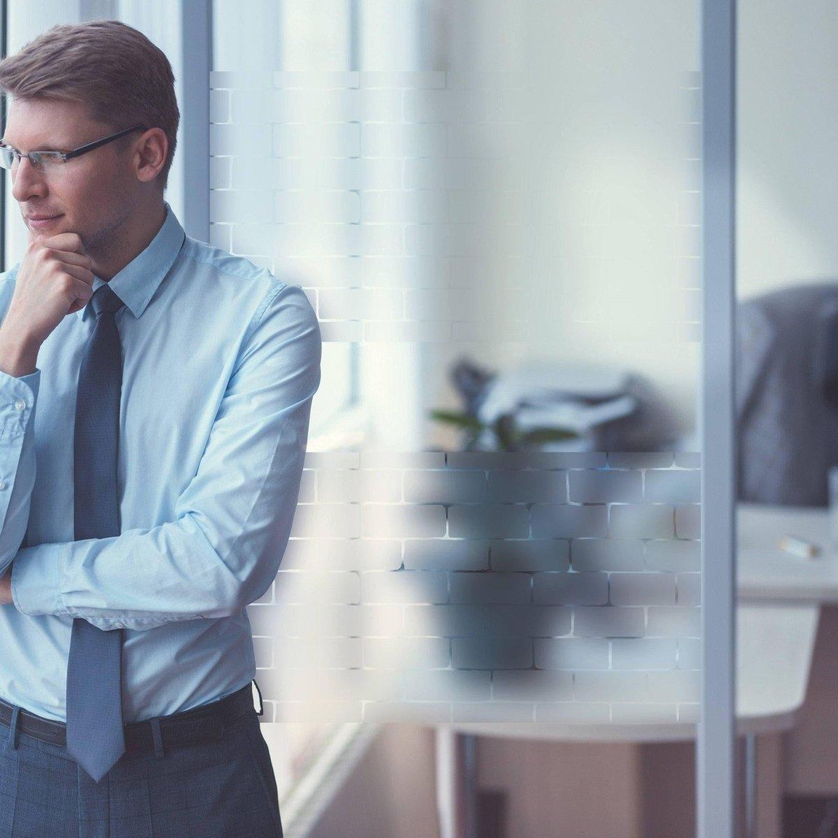 Professional man in a blue shirt and tie, thinking next to frosted window film for enhanced privacy and natural light.