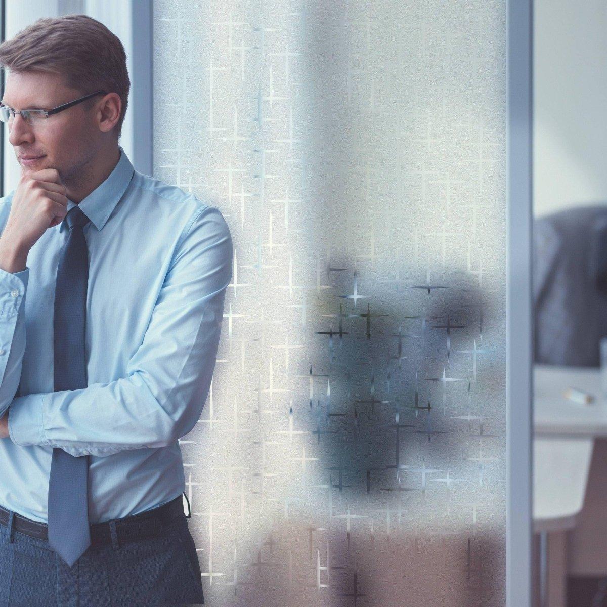 Businessman pondering beside a frosted film window decal for added privacy and style in an office setting.