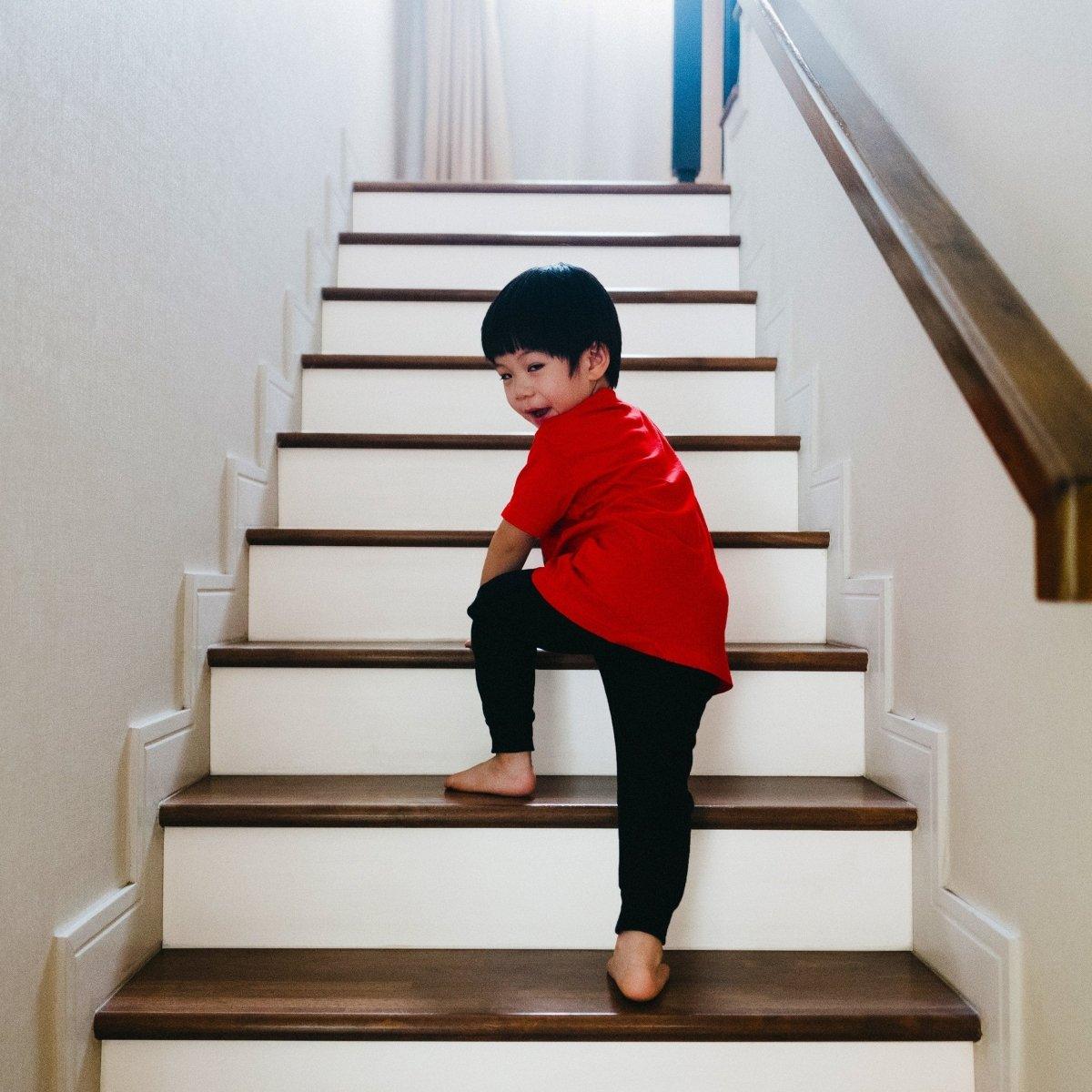 Child in a red shirt climbing white staircase with wood accents, showcasing a stylish home decor.