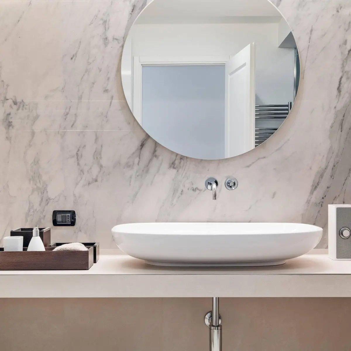 Modern bathroom with marble wall, stylish round mirror, and sleek white sink on a minimalist countertop.