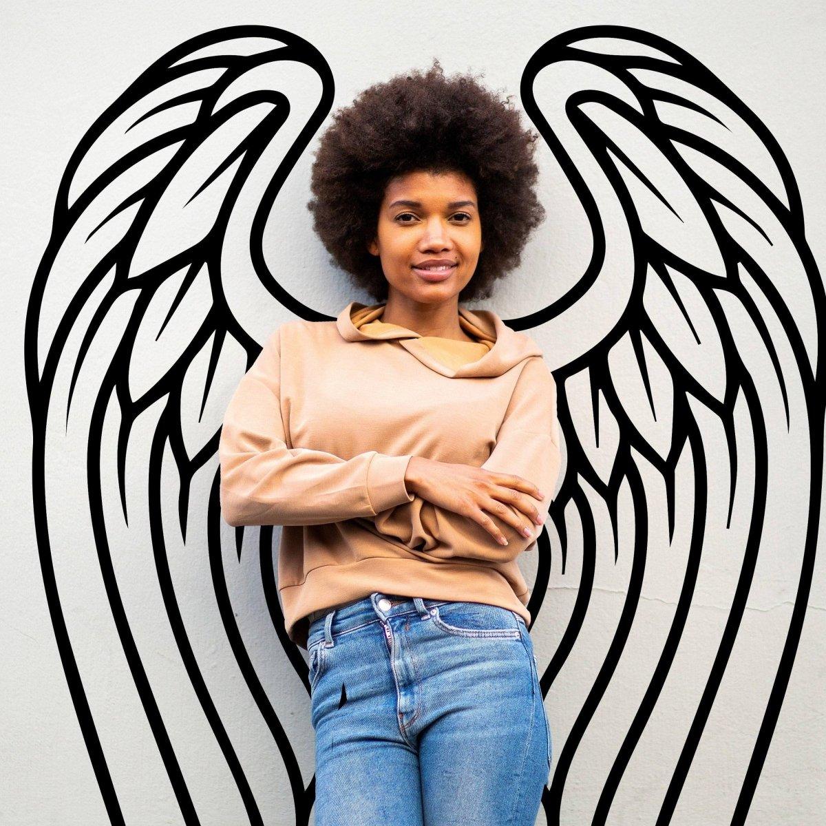 Young woman posing with angel wings wall decor in a stylish bohemian setting, showcasing artistic wall art.